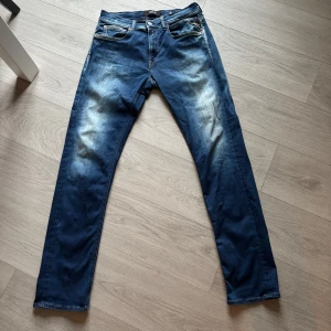 Replay Grover jeans blå, stl 32 - Snygga Replay Grover jeans i klassisk blå tvätt med slitningar och kontrastsömmar. Modellen har raka ben, fem fickor och läderpatch bak i midjan. Perfekta för dig som gillar en tidlös och avslappnad look storlek l34 w32