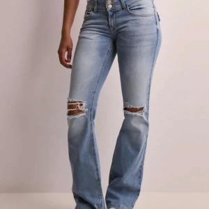 Ljusblå bootcut jeans med slitningar - Snygga ljusblå jeans med bootcut passform och slitna hål över knäna. Jeansen har hög midja, klassiska fickor och knäppning framtill. Perfekta för en avslappnad och trendig look. Bara använda en gång, så nästan helt nya, utan skavanker. Helt slutsåld storlek på hemsidan 