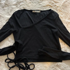 Svart omlottopp från NA-KD - Svart ribbad omlottopp från NA-KD med långa ärmar och knytband i midjan. Toppen har en snygg v-ringning och croppad passform. 
