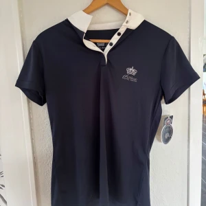 Marinblå Active Riding Wear tröja - Snygg marinblå pikétröja från Active Riding Wear med vit krage och knappslå. Tröjan har korta ärmar och broderad logga med krona på bröstet. Perfekt för ridning. Materialet är lätt och andas. Köpt på Ullared och aldrig använd. Har från samma märke och tycker dem är jättesköna och mjuka😍!Läs gärna bio💕 