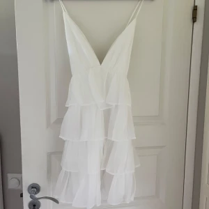 Vit volangklänning från Lulus - Min studentklänning! Supersöt vit kortklänning från Lulus med flera lager volanger och smala axelband. Djup v-ringning fram och korsade band bak. Endast använd under studentdagen. Nypris 1300