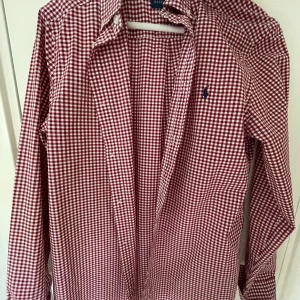 Rutig skjorta från Ralph Lauren  - Röd och vit rutig skjorta från Ralph Lauren i storlek XL. Klassisk krage, långa ärmar och knappar framtill. Skjortan har det ikoniska broderade logotypen på bröstet och är tillverkad i mjuk bomull. Perfekt för en stilren och avslappnad look. Passar för längden 170.
