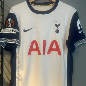 Tottenham Hotspur Bergvall matchtröja - Tottenham Hotspur fotbollströja med Bergvall och nummer 15 på ryggen. Vit med mörkblå ärmar, röda AIA-trycket på bröstet och officiella klubbmärken. Nike-logga på framsidan och Europa Conference League-märke på ärmen. Tillverkad i lätt och ventilerande material. Helt ny med tagg en replika 