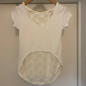 Vit topp med spetsdetaljer i ryggen - Vit topp med korta ärmar och rund hals. Baksidan har en längre, rundad nederkant i blommig spets som även syns upptill vid axlarna. T-shirten är i mjuk bomull och har en snygg kontrast mellan det enkla framstycket och den romantiska spetsen bak. Jättefint skick. Står ej märke eller strl men skulle uppskatta den som xs/ S och den är stretchig. Skriv för fler frågor eller funderingar. Läs bio. Kolla mina andra annonser också- pris går typ alltid att diskuteras!😇🙌