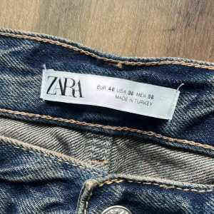 Rippade jeans från Zara med dragkedjor - Säljer ett par  jeans från Zara med rejält slitna och rippade detaljer på benen. Jeansen har dragkedjor vid bensluten och klassisk femficksdesign. De är tillverkade i denim och har en avslappnad passform med cool streetkänsla.