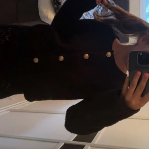 Svart cardigan jacka med guldknappar - Mysig svart cardigan jacka med lång ärm och snygga guldiga knappar framtill. Jackan har en rak passform och är tillverkad i ett fluffigt, stickat material som känns både trendigt och bekvämt. Perfekt att slänga på sig för en chill men ändå uppklädd look. Använd en gång innan och därför säljer jag den. Kontakta mig gärna om du har några frågor!😊