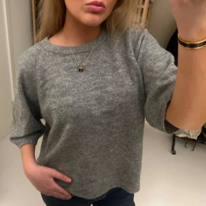 Grå stickad tröja med trekvartsärm - Mysig grå stickad tröja med trekvartsärmar och rund halsringning. Tröjan har en avslappnad passform och är perfekt att slänga på sig till jeans. Enkel och stilren design som funkar till många olika looks. Använd ett fåtal gånger!❤️