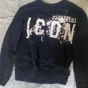 Svart Dsquared2 ICON sweatshirt L fast passar m också  - Svart sweatshirt från Dsquared2 i storlek L med stor vit 'ICON'-logga och stänkmönster framtill. Klassisk crewneck-modell med långa ärmar och ribbade muddar. Perfekt statement-plagg för dig som gillar streetwear och vill sticka ut.