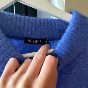 Blå stickad tröja Tiger of Sweden - Supermjuk blå stickad tröja från Tiger of Sweden i storlek XS. Tröjan har en klassisk rund halsringning med bred ribbad kant och långa ärmar. Perfekt för lager-på-lager och chill dagar. Enkel och stilren design som funkar till allt.