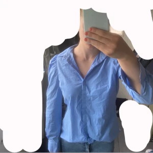 Blå skjorta från Second Female - Snygg blå skjorta från Second Female i klassisk modell med krage och långa ärmar. Skjortan har puffade axlar och knappar vid ärmslut. Tillverkad i bomull för en skön och luftig känsla. Perfekt till jeans eller kjol för en clean look eller elegant look.