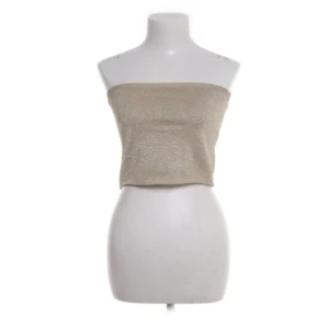 Glittrig champagnefärgad tubtopp från NA-KD - Snygg glittrig tubtopp i champagnefärg med bandeau-modell från NA-KD. Toppen är axelbandslös och har en lätt skimrande yta som fångar ljuset. Perfekt för dig som vill sticka ut med en enkel men ändå festlig look.