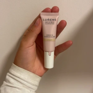 Lumene Invisible concealer färg LIGHT - Lumene Invisible Illumination Serum in Concealer i nyansen Light. Tuben är ljusrosa med vit kork och har en metallapplikator för enkel applicering. Perfekt för att täcka mörka ringar och ojämnheter med en naturlig finish.