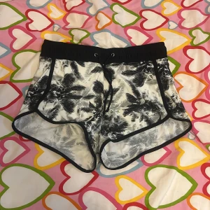 Svarta och vita badshorts med palmtryck - Snygga badshorts i svart och vitt med palmmönster och svarta kanter. De har elastisk midja med snörning och innerbyxa för extra komfort. Perfekta för stranden eller poolen, riktigt fräsch sommarstil!