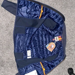 Mörkblå Parajumpers pufferjacka Y-M - Snygg mörkblå pufferjacka från Parajumpers med quiltad insida och coola orange detaljer. Jackan har dragkedja och klassisk PJS-logga på insidan. Perfekt för dig som vill ha en stilren och sportig look under höst och vinter.