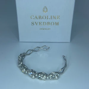 Caroline Svedbom silverarmband med pärlor - Snyggt armband i silverfärg från Caroline Svedbom med tvinnad design. Armbandet är dekorerat med gnistrande kristaller och små vita pärlor längs ovansidan. Fått den i studentpresent och säljer den då jag inte är en silvertjej, priset är 1000kr🫶🏽