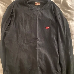 Svart långärmad tröja från Levi's - Svart långärmad tröja från Levi's med klassisk rund halsringning och liten röd Levi's-logga på bröstet. Enkel och stilren design som passar till det mesta. Tillverkad i mjuk bomull för skön känsla hela dagen.