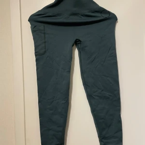 Mörkgröna tights från MM Sports - Mörkgröna tights från MM Sports med hög midja och en praktisk ficka på sidan. Tillverkade i mjukt och stretchigt material som passar perfekt för träning. Diskret logga tryckt vid midjan. Snygga och bekväma för dig som gillar att röra på dig.