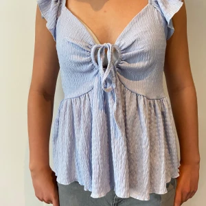 Ljusblå blus med knyt och volang - Gullig blå blus från lager 157 i strl XS. säljer då den inte kommer till användning bara använd några gånger.