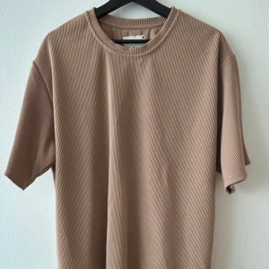 Beige ribbad t-shirt från Reserved - Säljer en stilren beige t-shirt från Reserved i storlek XL. T-shirten har en ribbad struktur och korta ärmar, perfekt för en avslappnad look. Passar bra till både jeans och shorts!