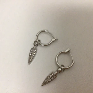 Silvriga örhängen med glittriga detaljer - Snygga silvriga örhängen med små glittriga stenar på en droppformad hängande detalj. Perfekta för att ge en extra touch av elegans till din outfit.