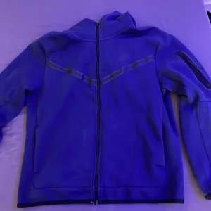 Blå fleecejacka från Nike - Säljer en blå fleecejacka från Nike med dragkedja framtill. Jackan har långa ärmar och en hög krage för extra värme. Perfekt för kyliga dagar.