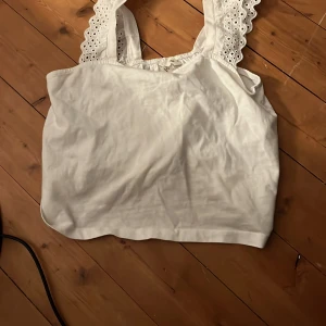 Vit ärmlös topp från H&M - Säljer en söt vit ärmlös topp från H&M med broderade axelband. Perfekt för varma dagar eller som ett lager under en kofta. Toppen har en luftig passform och är tillverkad i ett mjukt material.