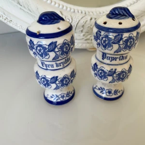 Blåvita kryddburkar med blommönster - Charmiga vintage kryddburkar i keramik med blått blommönster och text för 'Fyra kryddor' och 'Paprika'. De har en unik form med blå detaljer och hål i locket för enkel dosering. Perfekt för att ge köket en vintagekänsla.längd är 10cm båda för 100kr
