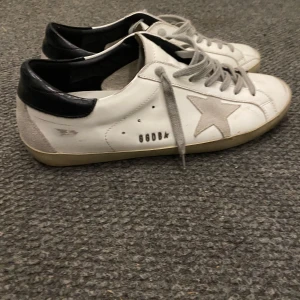 Golden goose - Snygga vita sneakers från Golden Goose med en grå stjärna på sidan och svarta detaljer vid hälen. Skorna har grå snörning och en klassisk design som passar perfekt för en avslappnad stil.