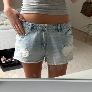 Ljusa jeansshorts med slitningar - Säljer ett par ljusa jeansshorts från Levi's med coola slitningar framtill. Shortsen har en klassisk femficksdesign och knappgylf. Perfekta för en avslappnad sommarlook!