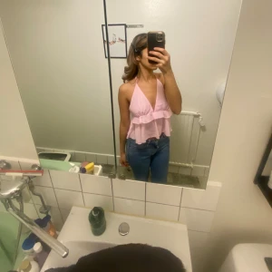 Rosa ärmlös topp med volang - Säljer en söt rosa ärmlös topp med volangdetaljer. Toppen har en halterneck-design och öppen rygg, vilket ger en luftig och somrig känsla. Perfekt för varma dagar!