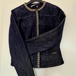 Mörkblå jeansjacka från Liu Jo - Snygg mörkblå jeansjacka från Liu Jo med kedjedetaljer längs krage och dragkedja. Jackan har en stilren design med långa ärmar och två framfickor. Perfekt för att ge din outfit en cool touch. Den är storlek 42 men känns som 38-40. Går ej att förhandla, priset är fast 