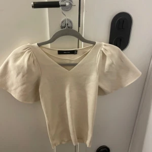 Beige topp från Vero Moda  - Säljer en stilren beige topp från Vero Moda med puffiga kortärmar och v-ringning. Perfekt för en chic och enkel look.