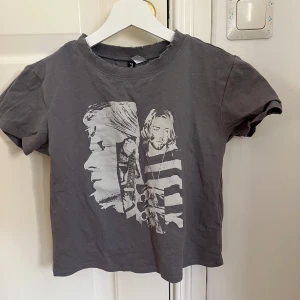 Grå t-shirt med tryck från H&M Divided - Säljer en grå t-shirt från H&M Divided med ett coolt tryck av två ansikten i vitt. T-shirten har en rund hals och korta ärmar, perfekt för en avslappnad stil. Passar bra till jeans eller shorts för en casual look.