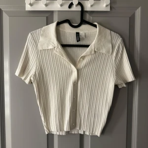 Vit ribbad kortärmad blus  - Säljer en stilren vit ribbad blus från H&M med korta ärmar och knappar framtill. Den har en klassisk krage och är i en mjuk och bekväm kvalitet.