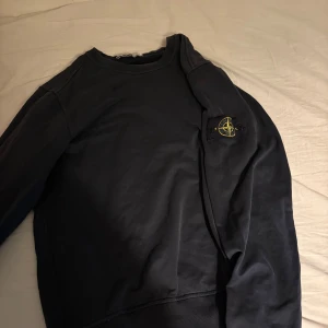 Svart tröja från Stone Island - Säljer en svart tröja från Stone Island med rund hals och lång ärm. Tröjan har en ikonisk logotyp på ärmen. Perfekt för en stilren och avslappnad look. Den är i mycket bra skick, och såklart äkta! Är öppen för byten och pris kan diskuteras vid snabbaffär!