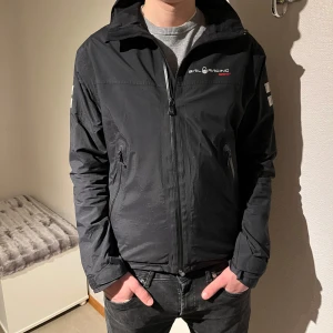 Svart vindjacka från Sail Racing - Säljer en svart vindjacka från Sail Racing med dragkedja och broderad logga på bröstet. Jackan har långa ärmar och praktiska fickor med dragkedja. Perfekt för blåsiga dagar.               Nypris 2300kr