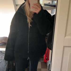 Svart teddyjacka från Carin Wester - Mysig svart teddyjacka med dragkedja framtill. Jackan har en oversized passform och långa ärmar, perfekt för kyligare dagar. Den fluffiga texturen ger en trendig look. Märket är Carin Wester, slutsåld, nypris 800kr