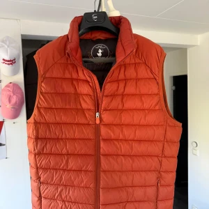 Orange dunväst  - Säljer en orange dunväst från Save The Duck i fint skick. Västen är quiltad och har en dragkedja framtill. Den är tillverkad av syntetiskt material och Plumtech-teknologi för värme och andningsförmåga. Perfekt nu till våren, nypris 1499kr snabb affär 500kr Size M/L