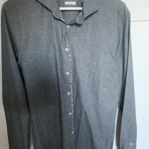 Grå skjorta från Bruun & Stengade - Snygg grå skjorta från Bruun & Stengade med diskreta knappar och en stilren design. Perfekt för en elegant look. Skjortan har långa ärmar och en klassisk krage.