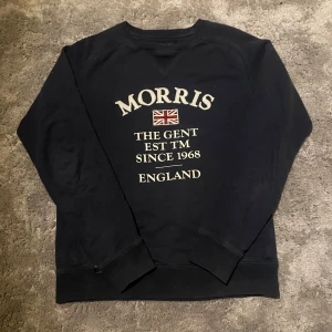 Morris tröja - Snygg svart sweatshirt från Morris med text och brittisk flagga på framsidan. Perfekt för en avslappnad stil med långa ärmar och rund halsringning.