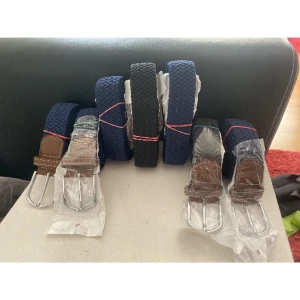 Blå och svarta bälten - Säljer flera snygga bälten i blått med bruna detaljer. Bältena har en flätad design och är perfekta för att ge en stilren touch till din outfit. Spännena är i silverfärg och ger en klassisk look.