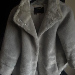  trekvartsärmad pälsjacka - Elegant grå pälsjacka från Nenette med en lyxig känsla. Jackan har en klassisk krage och stängs med diskreta knappar. Perfekt för att hålla sig varm och stilfull under kyliga dagar.