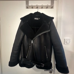 Svart jacka från Pieces - Snygg svart jacka från Pieces med dragkedja och bälte. Jackan har en klassisk design med långa ärmar och en mjuk insida. Perfekt för vår väder! Knappt använd.