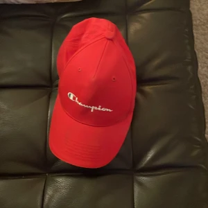 Röd keps från Champion - Snygg röd keps från Champion med broderad logga framtill. Perfekt för en sportig look eller som en stilren accessoar. Justerbar passform för optimal komfort.