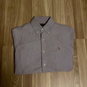 Beige skjorta från Polo Ralph Lauren - Snygg beige skjorta från Polo Ralph Lauren i slim fit. Skjortan har knappar framtill och en broderad logotyp på bröstet. Perfekt för en stilren look. Kolla gärna in butiken, det finns möjlighet för bundle.