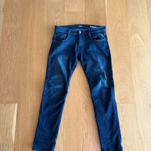 Mörkblåa replay anbass jeans - Snygga blå jeansbyxor från Replay i modellen Anbass. De har en slim fit och klassisk femficksdesign med dragkedja. Perfekta för en stilren look. Inga defekter på jeansen!