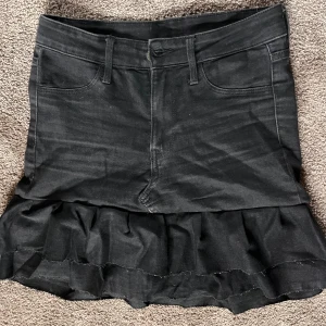 Svart jeanskjol med volang - Snygg svart/grå jeanskjol med volangdetaljer längst ner. Strl 36💛