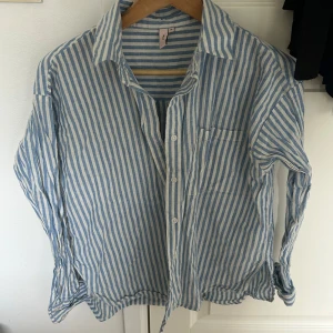 Blå- och vitrandig skjorta från Nelly - Säljer en stilren blå- och vitrandig skjorta från Nelly. Skjortan har långa ärmar och knappar framtill. Perfekt för en avslappnad och trendig look.