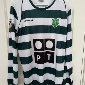 Randig fotbollströja från Reebok - Säljer en klassisk randig fotbollströja från Reebok med Sporting CP:s emblem på bröstet. Tröjan är vit och grön med långa ärmar och har nummer 28 och namnet C. Ronaldo på ryggen. Perfekt för samlare eller fans av laget!