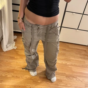 Beige cargobyxor med snörning - Snygga beige cargobyxor med flera fickor och justerbar snörning vid bensluten. Byxorna har en loose fit och är perfekta för en avslappnad stil. De har en låg midja och är tillverkade i ett bekvämt material.